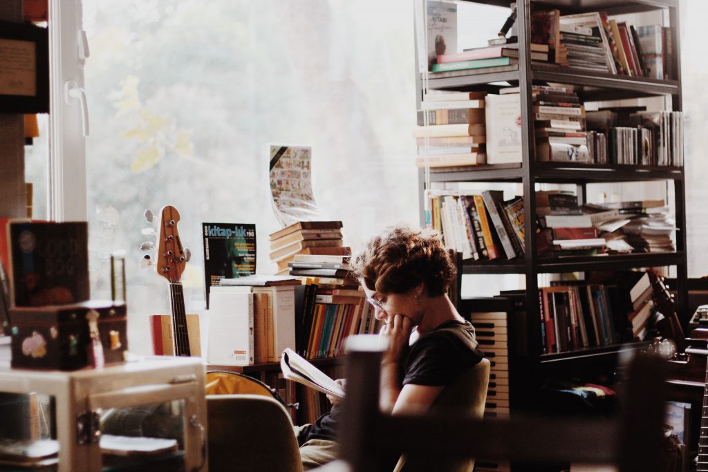 A woman reads a book near the window of a well-lit room